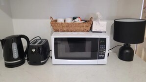 A kitchen counter with a microwave, toaster, kettle, and a lamp. - Spacious Room (Grange)