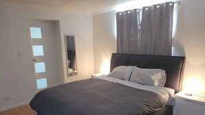 A bedroom with a large bed, a nightstand, a wall-mounted mirror, and a window with curtains. - Spacious Room (Grange)