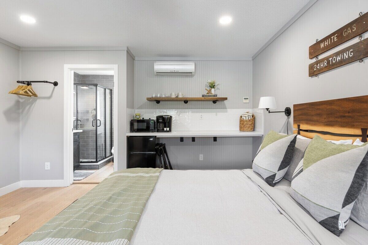 Habitación de hotel pequeña con cama, kitchenette, ducha y un letrero que indica servicio de remolque disponible las 24 horas.