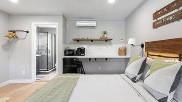 Habitación de hotel pequeña con cama, kitchenette, ducha y un letrero que indica servicio de remolque disponible las 24 horas.