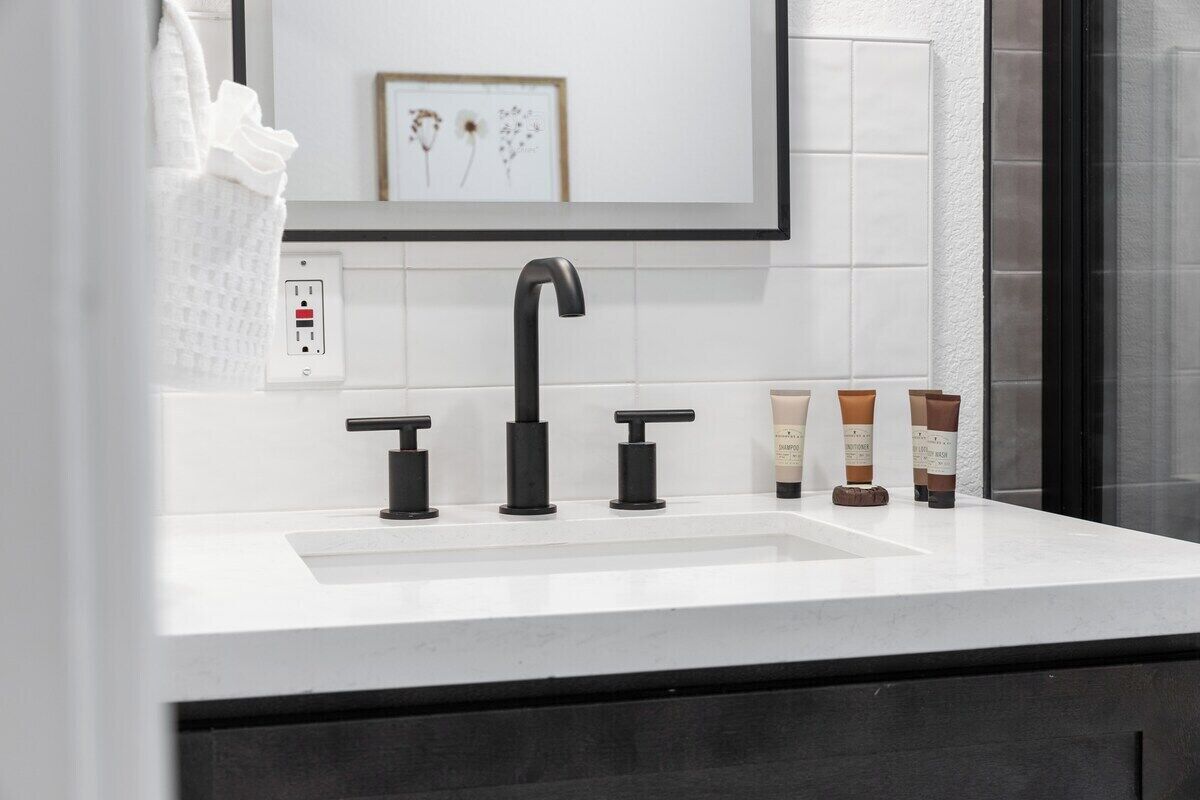 A bathroom with a white sink, black faucet, and three toiletries.