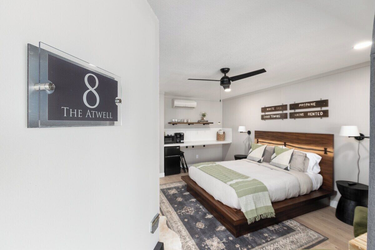 Een moderne slaapkamer met een groot bed, een plafondventilator en een kleine keuken in de achtergrond.