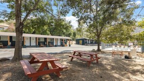 Un motel con mesas de picnic al aire libre, una zona de piscina y un patio de recreo cercado.