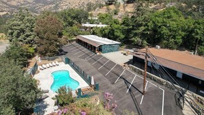 Un hotel con piscina, estacionamiento y montañas al fondo.