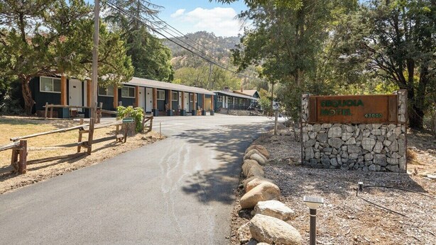 Un motel con un letrero de piedra, un camino de entrada pavimentado y una hilera de cabañas.