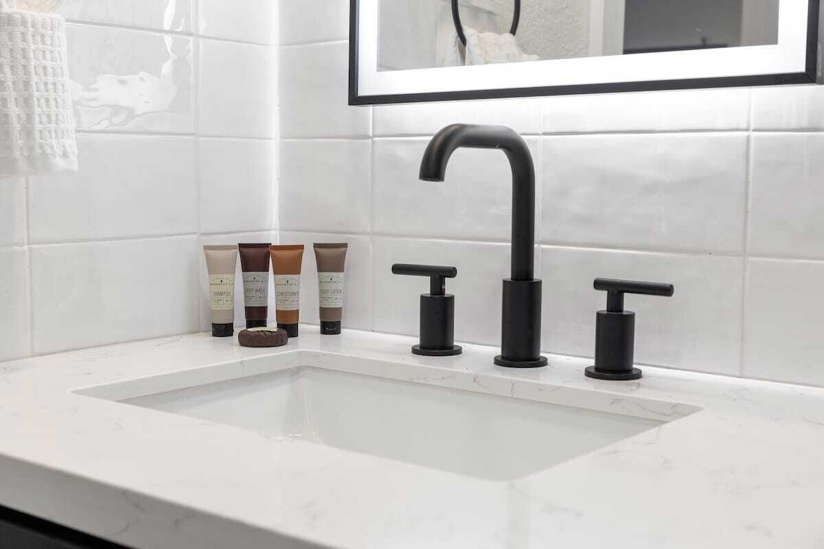 A bathroom with a white sink, black faucet, and two soap dispensers.