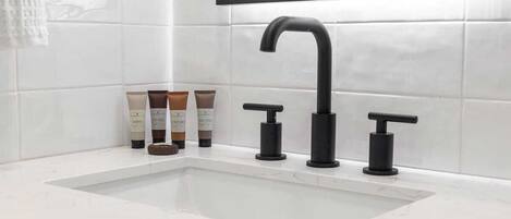 A bathroom with a white sink, black faucet, and two soap dispensers.