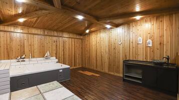 A wooden-paneled room with a large sink, a small boat decoration, and a shelf with bottles.