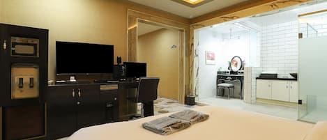 A hotel room with a bed, a desk with a computer, a television, and a bathroom visible through an open door.