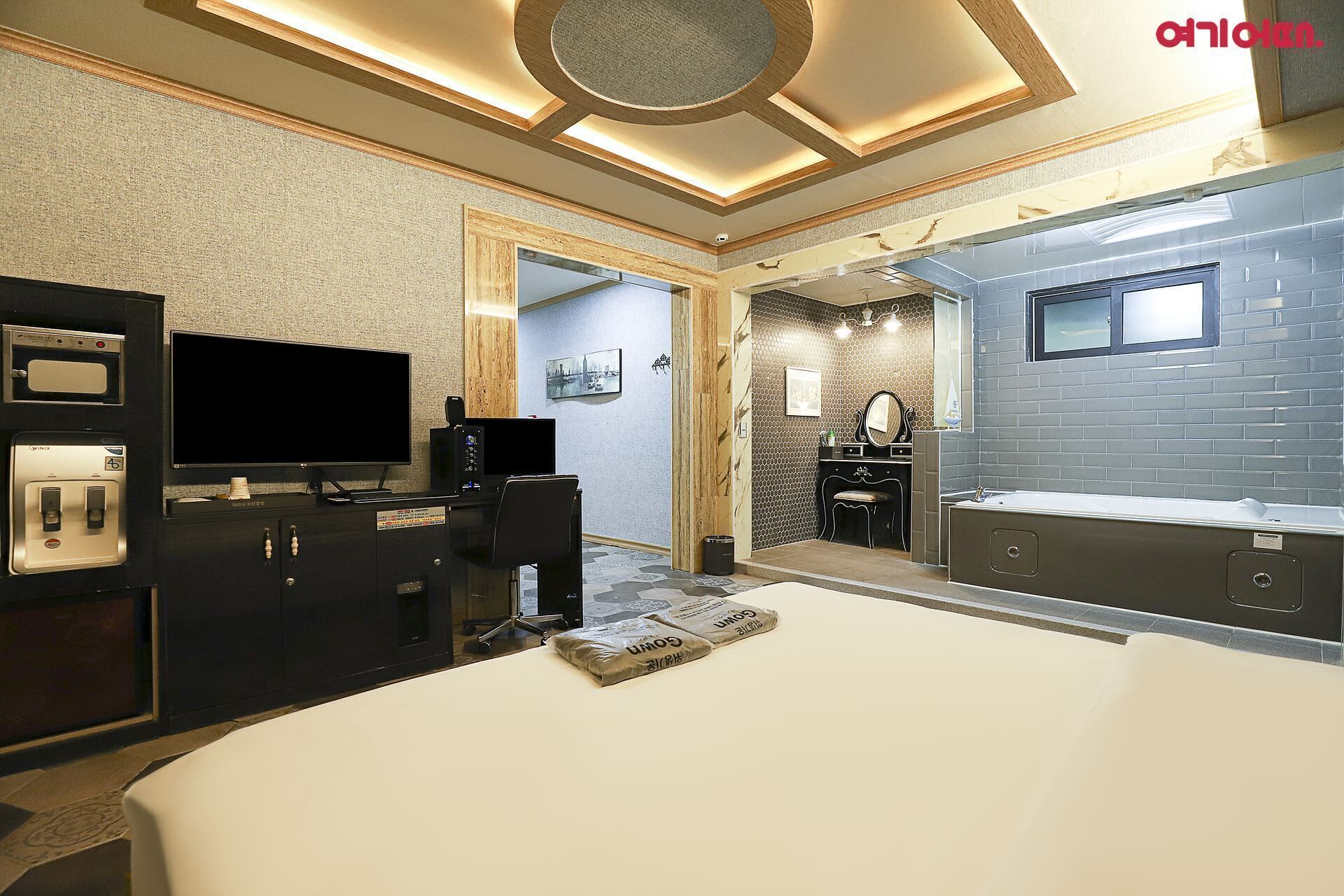 A modern hotel room with a large bed, a desk with a computer, a television, and a bathroom with a bathtub and sink.