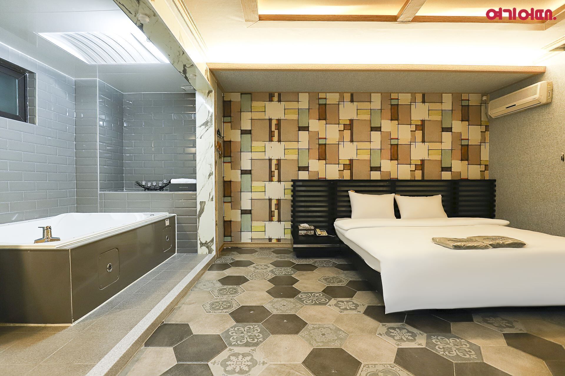 Quarto de hotel moderno com banheiro, uma cama e um painel de cabeceira estampado, e piso revestido de azulejos.