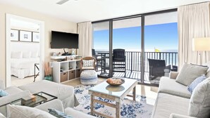 A modern living room with a large TV, a sofa, a coffee table, and a balcony with a view of the sea. - Newly Updated 2BR Beachfront Condo With Balcony and Direct Beach Access (Santa Rosa Beach)