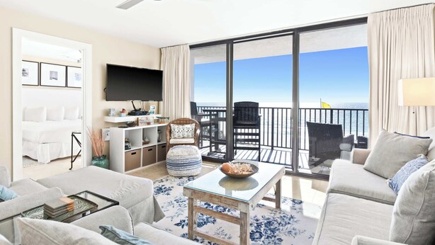 A modern living room with a large TV, a sofa, a coffee table, and a balcony with a view of the sea. - Newly Updated 2BR Beachfront Condo With Balcony and Direct Beach Access (Santa Rosa Beach)