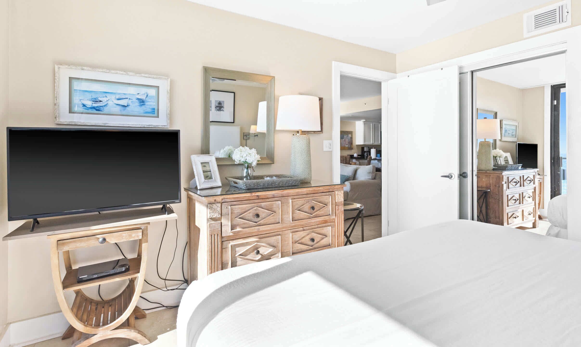 A hotel room with a bed, a TV, a dresser, and a bathroom visible through an open door.