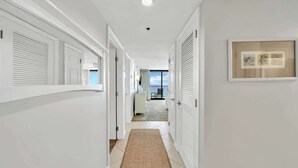 A hallway with white walls, a tiled floor, and a framed picture on the wall.