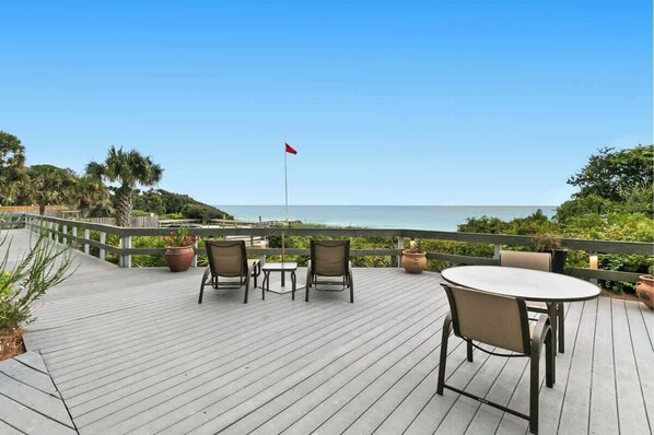 A wooden deck with a table and chairs, overlooking a beach with a flag.