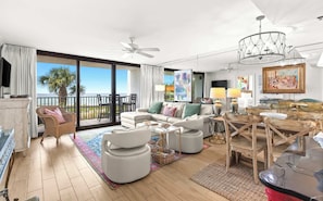 A spacious living room with a balcony, a ceiling fan, and a chandelier.
