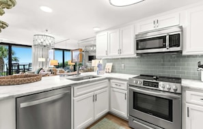 A modern kitchen with white cabinets, stainless steel appliances, and a large window overlooking a balcony.