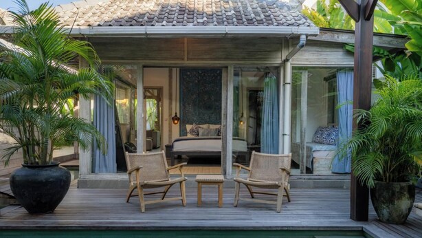 A poolside area with a bed, two wicker chairs, and large potted plants. - Mundaka Villa by Betterplace (Canggu)
