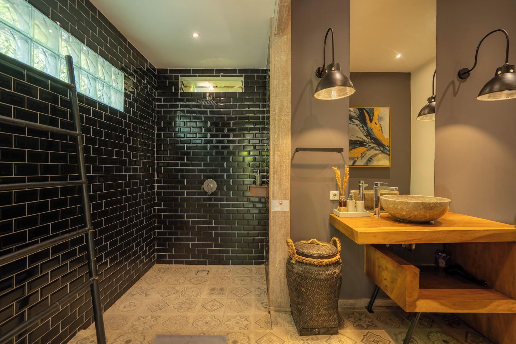 A bathroom with a black tiled shower, a wooden vanity, and a hanging light fixture.