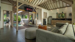A spacious living area with a modern kitchen, a visible Netflix sign, and a large window overlooking greenery. - Mundaka Villa by Betterplace (Canggu)