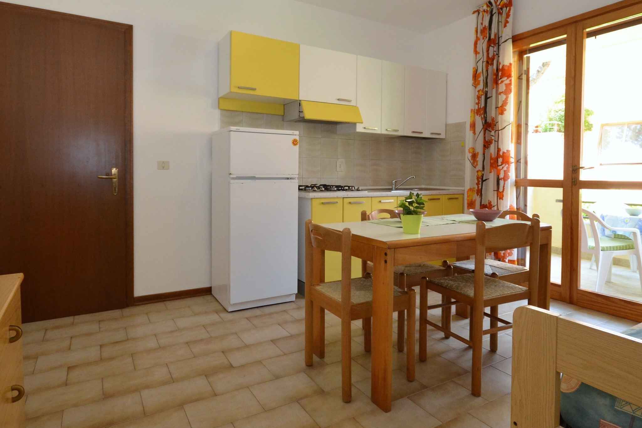 A compact kitchen with a refrigerator, stove, and yellow cabinets. There is a dining table with chairs and a window with curtains.