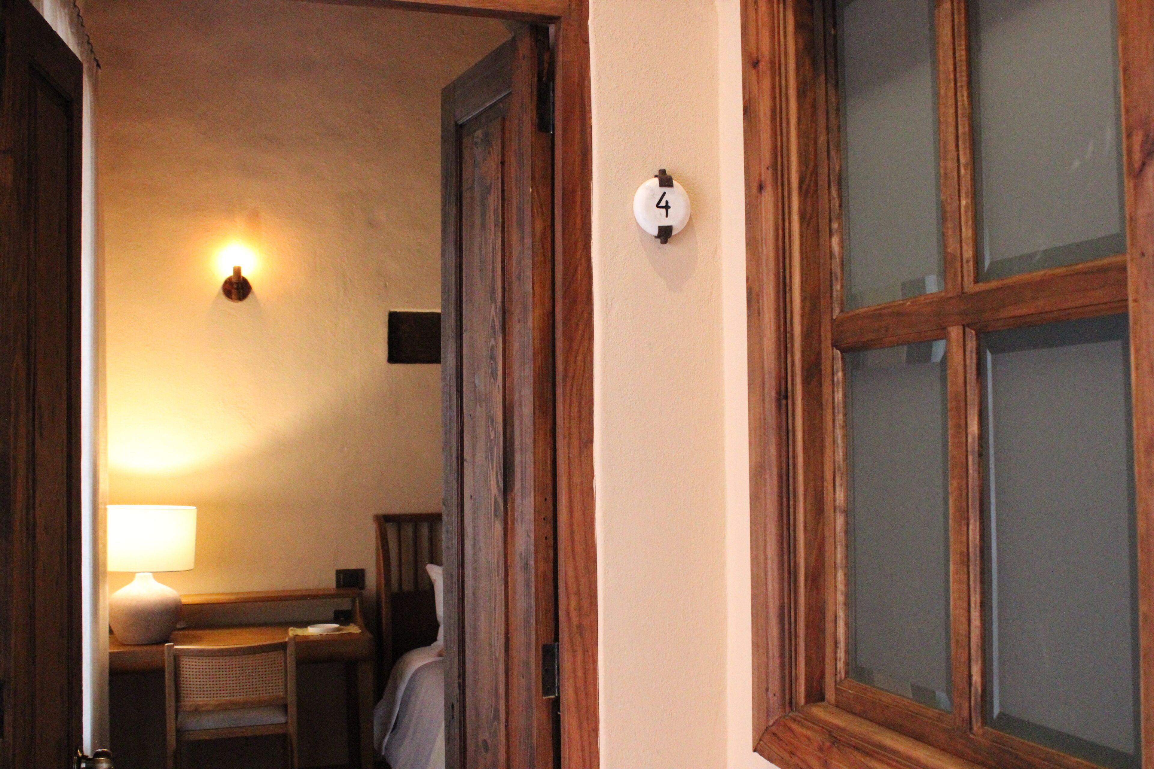 A room with a wooden door, a number '4' sign, a lamp, a chair, and a bed.