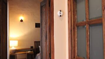 A room with a wooden door, a number '4' sign, a lamp, a chair, and a bed.