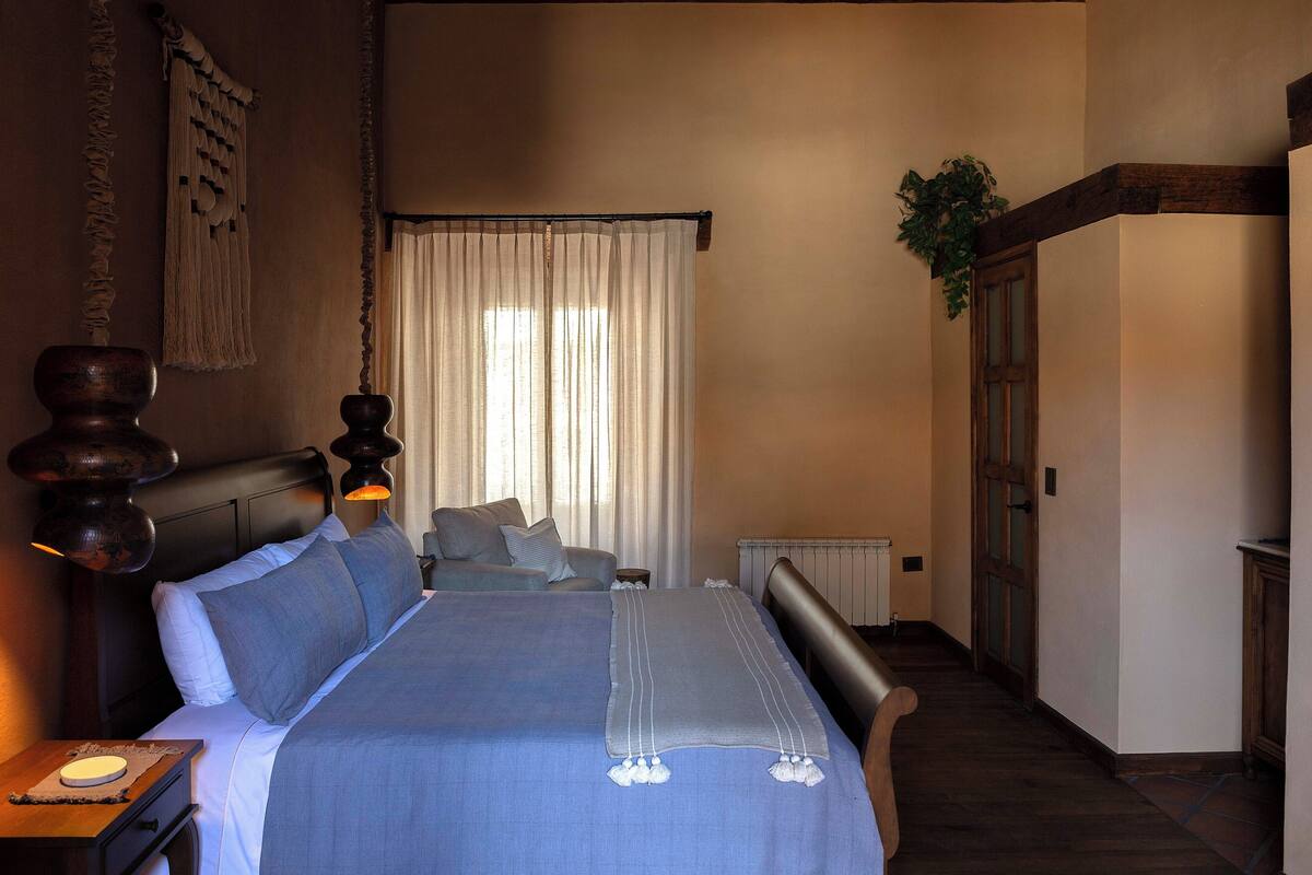 A bedroom with a bed, bedside table, lamp, curtains, and a radiator.