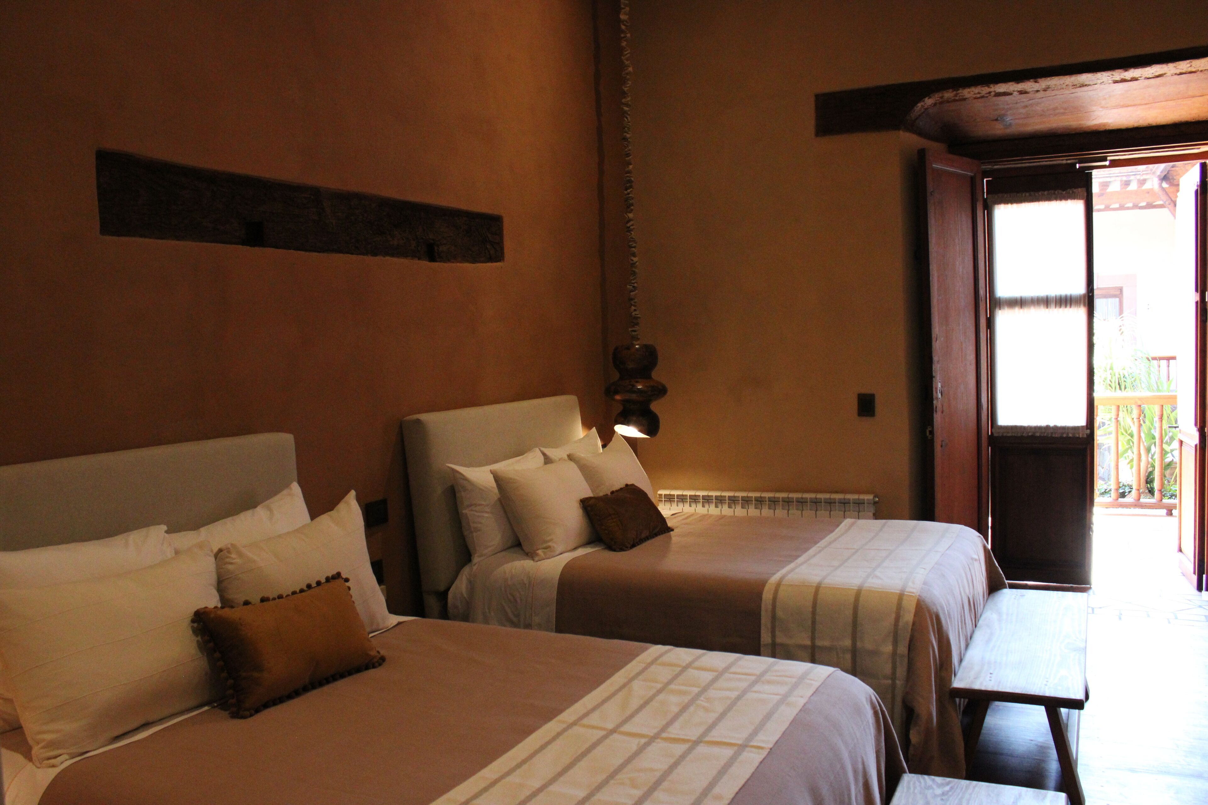 Two beds with headboards, a wooden bench, and a view of the outside.