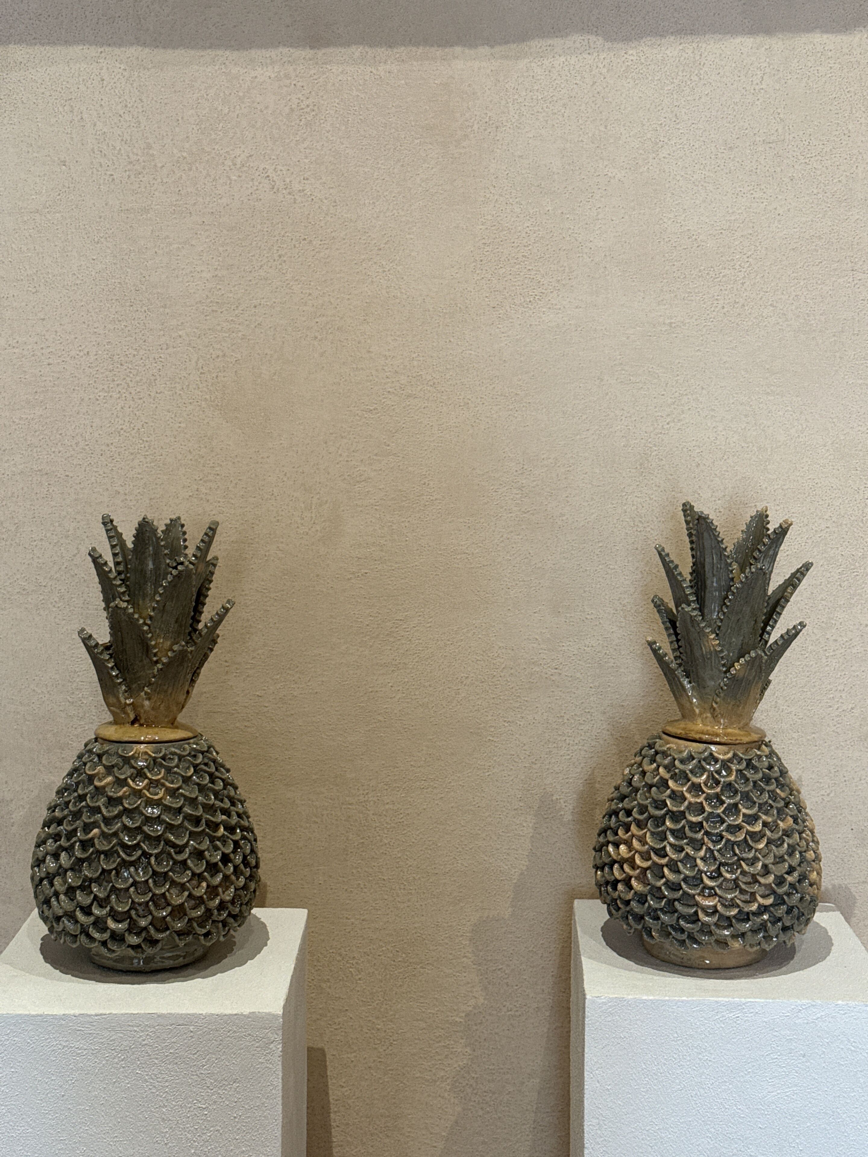 Two decorative pineapple sculptures on white pedestals against a textured wall.
