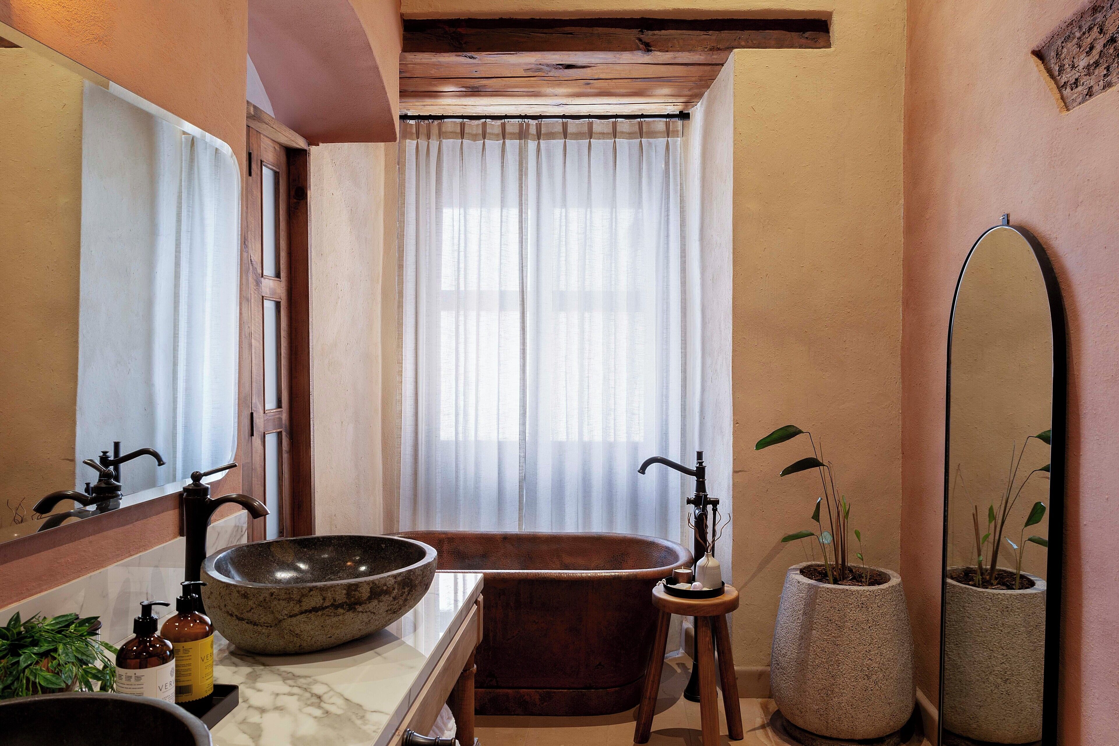 Un baño con una bañera independiente, un lavamanos grande, un espejo y una planta en maceta.
