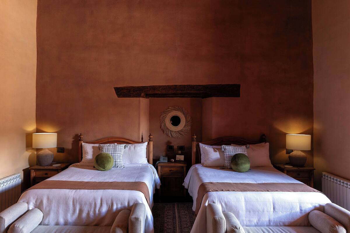 A hotel room with two single beds, a wooden ceiling beam, a round mirror, and bedside lamps.