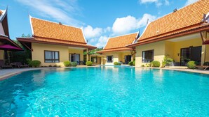A swimming pool with adjacent buildings, clear skies, and a calm water surface. - Kana Hotel Phuket (Rawai)