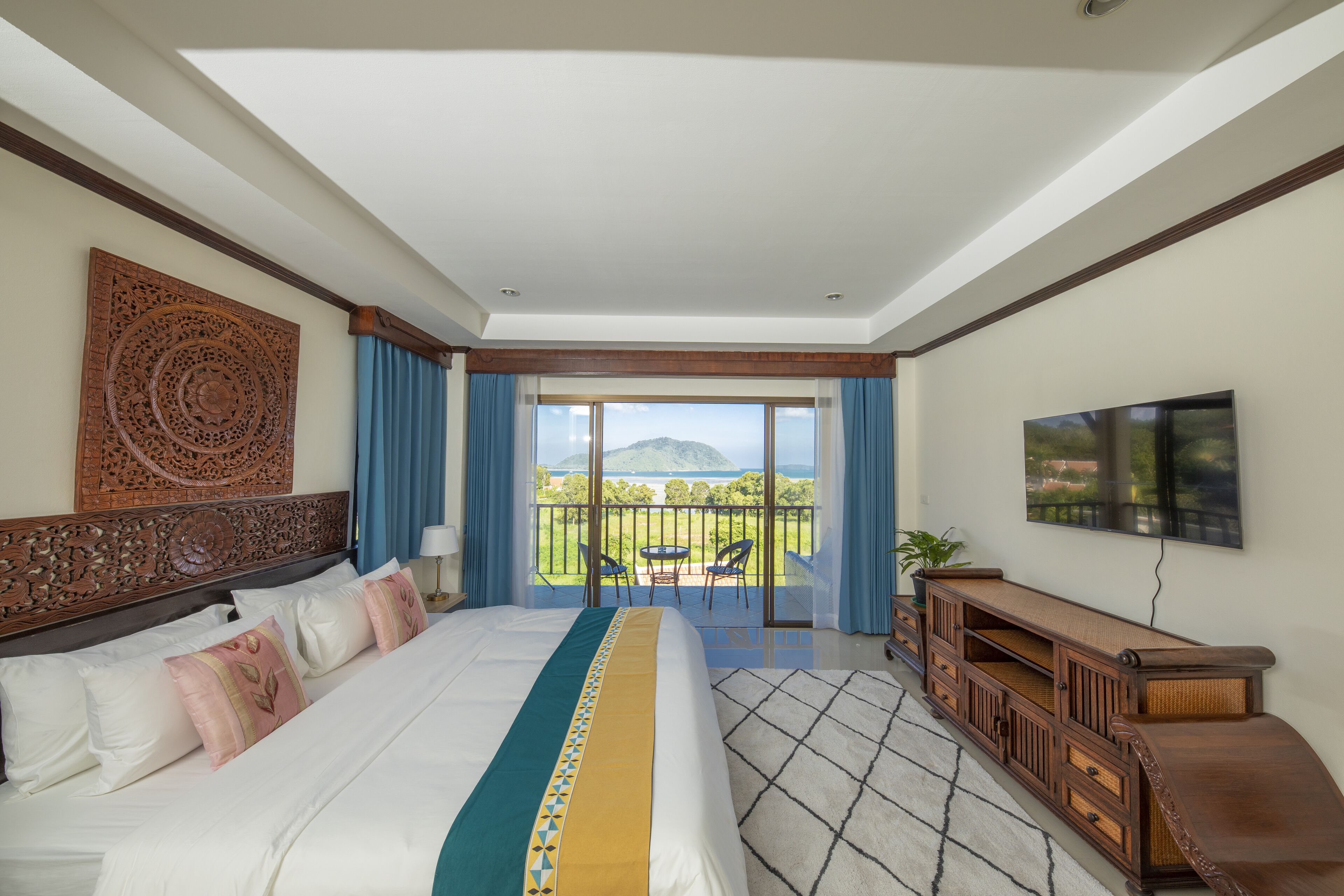 A bedroom with a large bed, a TV, a balcony with a view, and a wooden console table.