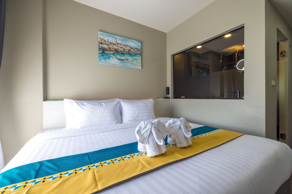 A hotel room with a bed, a painting on the wall, and a bathroom mirror.
