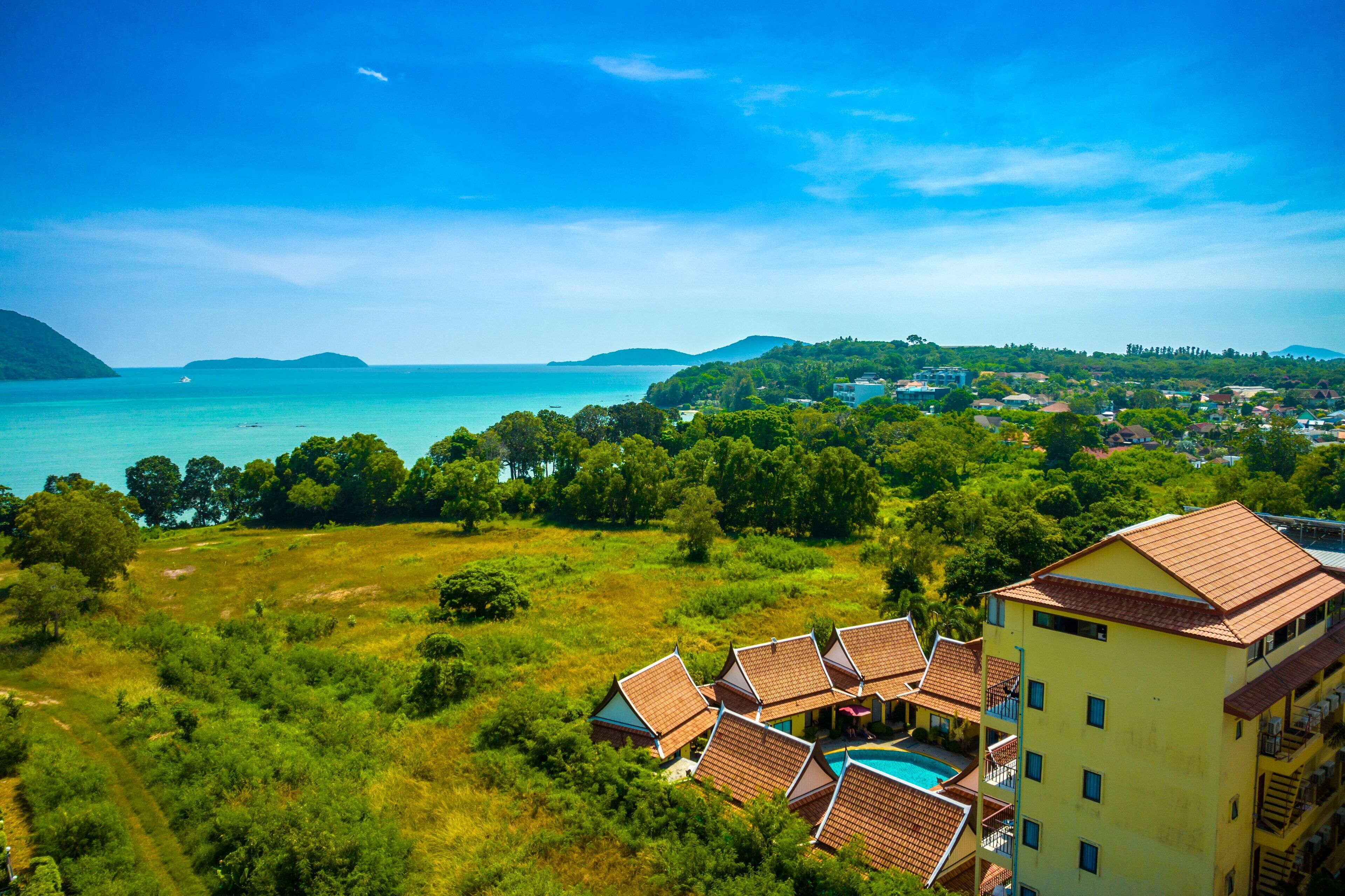 A coastal resort with multiple buildings, a swimming pool, and a view of the sea and hills.