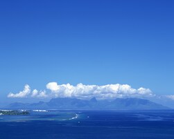 A coastal landscape with a clear sky, calm sea, and distant mountains.