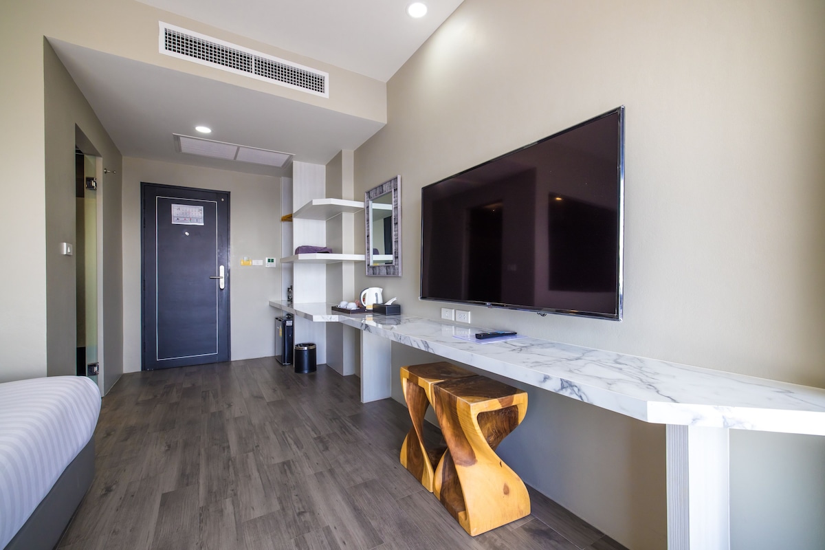 A modern hotel room with a bed, a wooden stool, a marble countertop, a TV, and a door with a security panel.