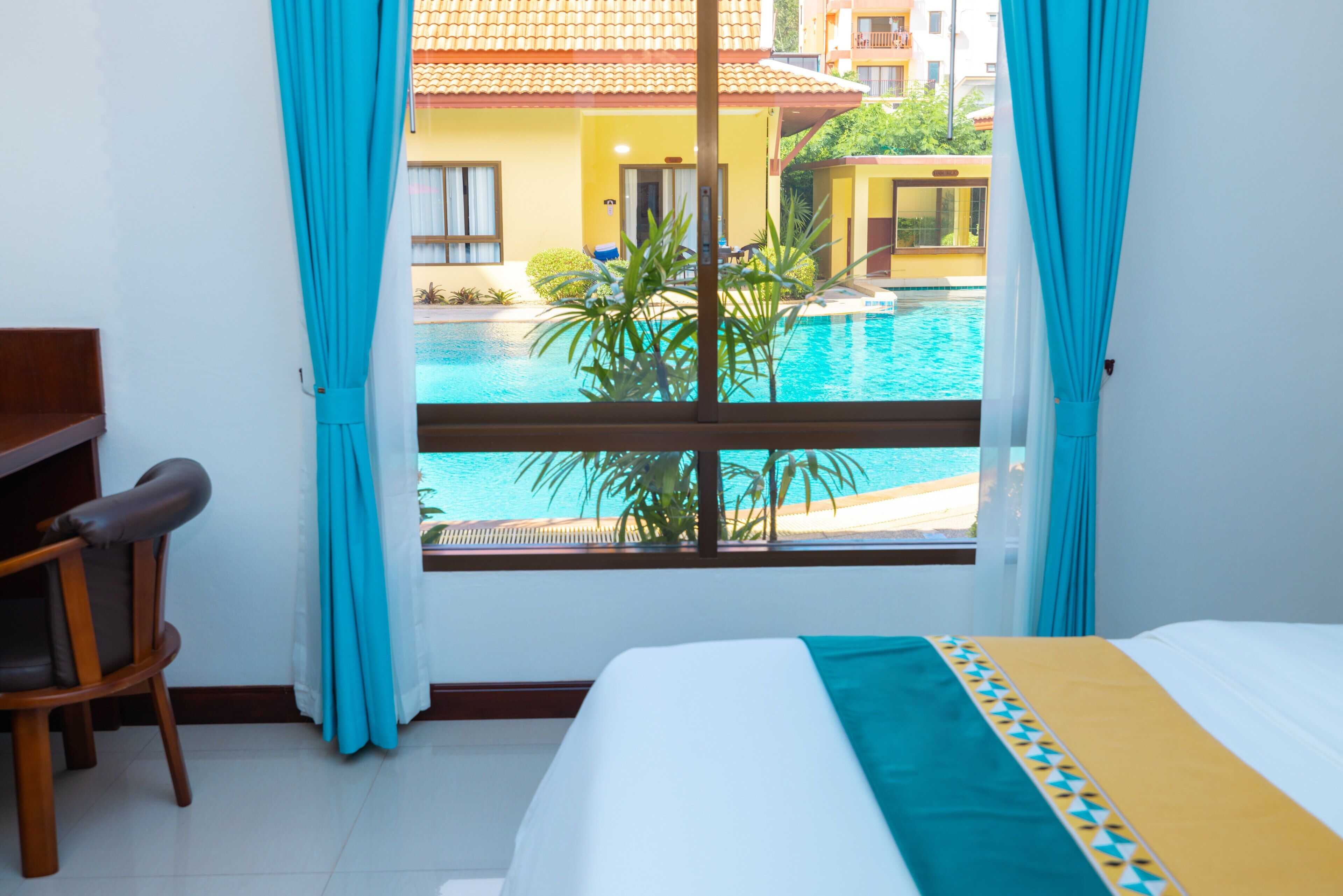 Habitación de hotel con cama, escritorio y vista a una piscina y edificios.