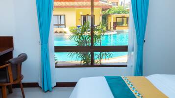 Habitación de hotel con cama, escritorio y vista a una piscina y edificios.