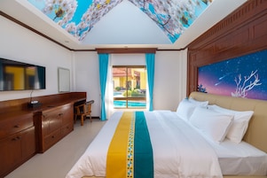A hotel room with a bed, wooden desk, and a view of the pool through a glass door.