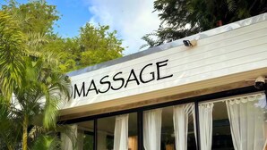 A massage parlor with a sign, large windows with white curtains, and tropical plants outside. - Kana Hotel Phuket (Rawai)
