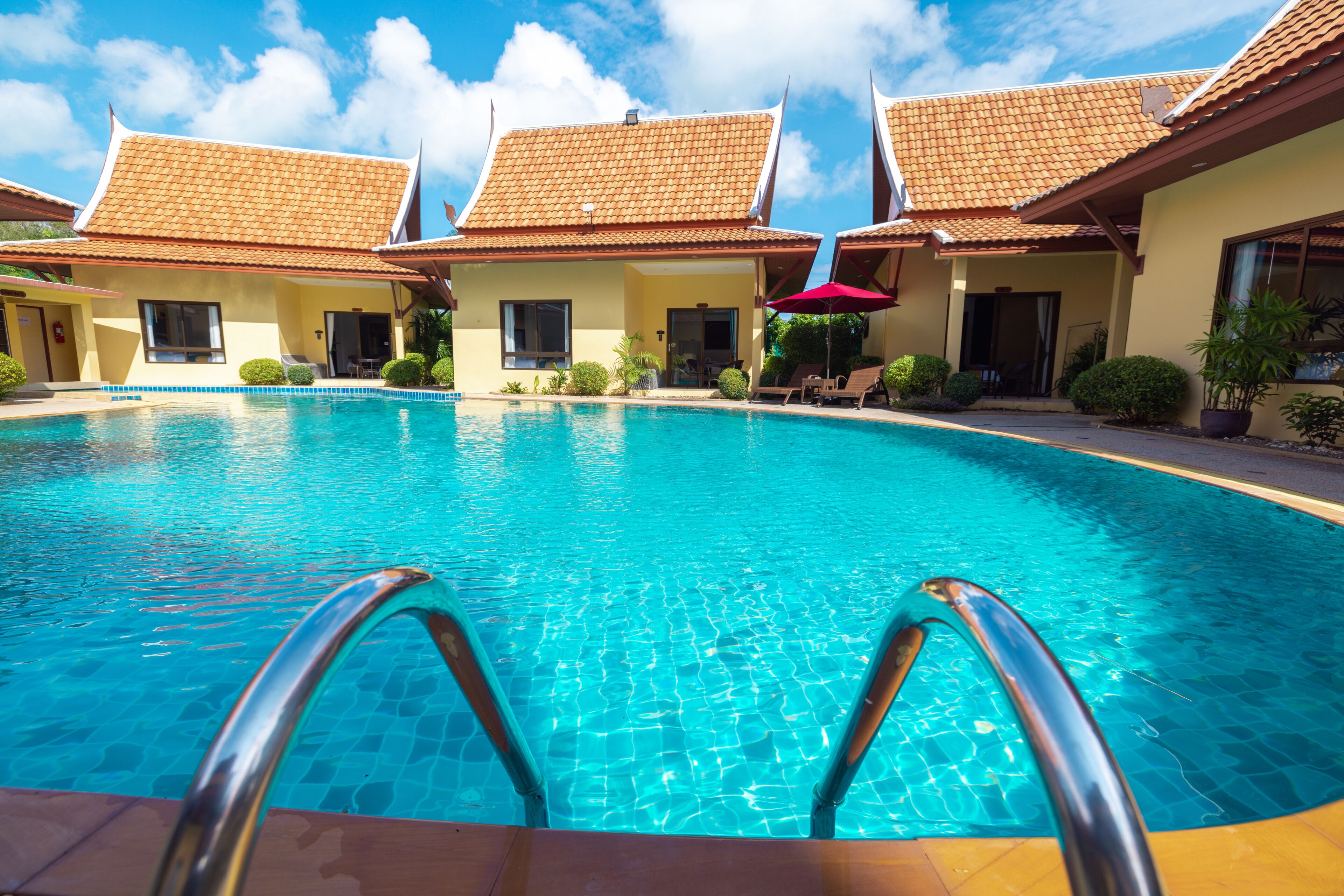 A swimming pool with clear water, surrounded by buildings with tiled roofs and a clear sky.