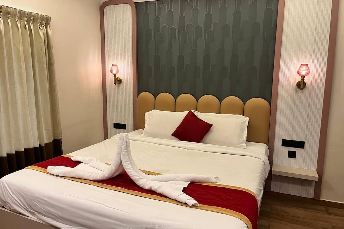 A hotel room with a neatly made bed, a red throw blanket, and a towel on the bed.