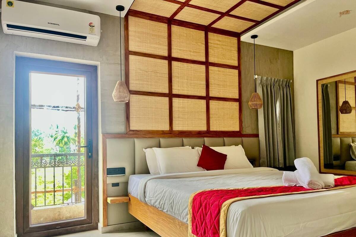 A hotel room with a bed, a window, a door, and an air conditioning unit.