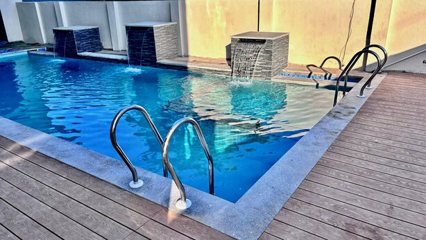 A swimming pool with a wooden deck, metal handrails, and a stone waterfall feature. - Hotel Castle Manor (Vanur)