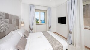 A hotel room with a bed, curtains, a TV, and a window with a view. - Villa Francy, Exclusive Villa on the sea with pools (Praiano)