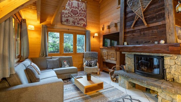 A cozy log cabin interior with a stone fireplace, a sofa, and a TV mounted on the wall. - Chalet Glaciers | Fireplace | View | Comfy | Quiet (Les Houches)
