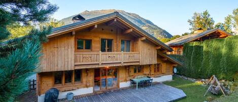 A wooden chalet with a balcony, a patio, and a mountain backdrop.